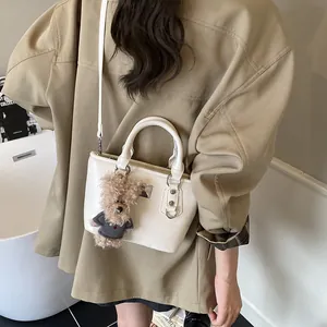 Chic beige bucket bag with plush bear charm and crossbody strap for stylish commuting