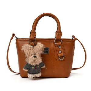 Brown leather bucket bag with top handles, silver hardware, and plush dog pendant