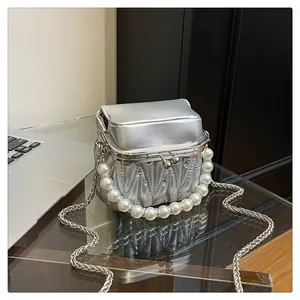 Detail der silbernen gesteppten Mini-Tasche mit Perlengriff und Metallkette auf Glas