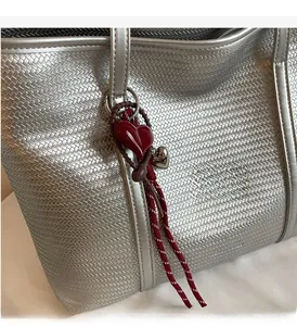 Detail of silver woven tote bag featuring a burgundy heart charm and metallic texture
