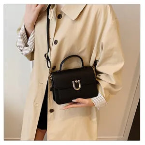 Détail d'un sac à main noir à motif litchi avec boucle fer à cheval sur un manteau beige