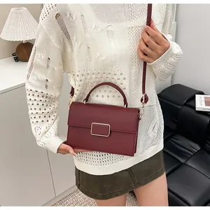 Sac bandoulière en cuir bordeaux avec boucle dorée porté par un mannequin élégant