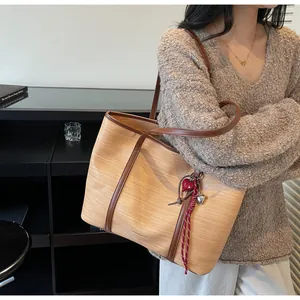 Detail of light brown woven tote bag featuring brown leather trim and red heart charm