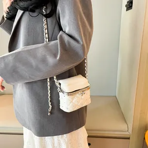 Weiße gesteppte Mini-Kettentasche mit Kristallbesatz, getragen von einem Model im Innenraum