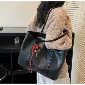 Detail of black tote bag featuring woven texture and red heart rope charm accessory