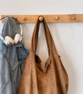 Detail of dark brown matte tote bag with wide shoulder strap on wooden wall hook