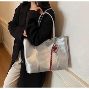 Detail of silver woven tote bag featuring a metallic texture and a red heart charm