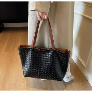 Detailed view of black hand-woven tote bag with brown handles on a light trench coat