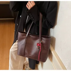 Detail of dark brown tote bag with woven texture, heart charm and long shoulder straps