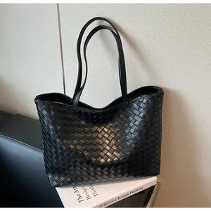 Close-up of black hand-woven tote bag with intricate intrecciato texture on white books