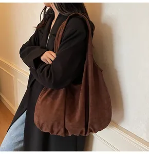 Detail of a large dark brown suede hobo tote bag with pleated base on a female model