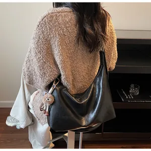 Detail of a black leather hobo bag with sleek finish and a brown plush charm accessory