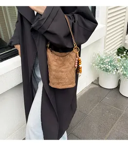 Detail der braunen Wildleder-Eimertasche mit Steppmuster und Ethno-Perlenanhänger