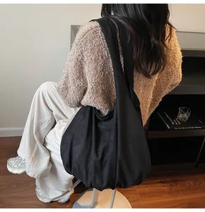 Black oversized suede hobo tote bag with wide shoulder strap shown on a model