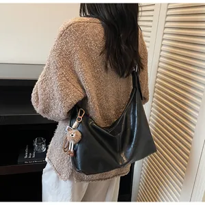 Detail of a black large-capacity crescent shoulder bag featuring a cute teddy bear charm