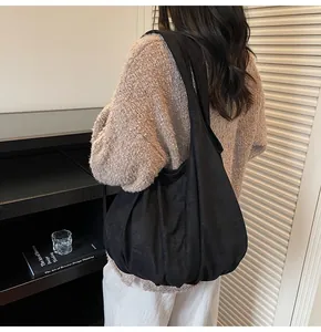 Detail of a black matte tote bag with wide straps and elegant bottom pleats worn by a model
