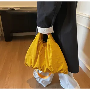 Detail view of large yellow nylon tote bag with pleated texture on a shoulder strap