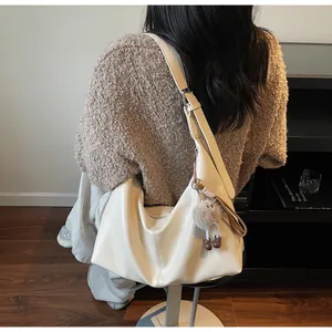 Detail of a large cream tote bag with a soft plush doll pendant and wide strap