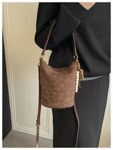 Detail der dunkelbraunen Wildleder-Beuteltasche mit Steppmuster und Vintage-Perlenanhänger