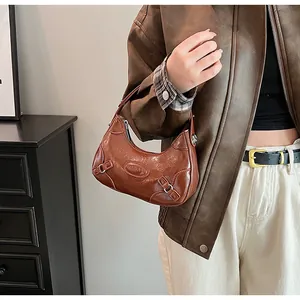 Detail of a brown crescent hobo bag with glossy leather texture and vintage buckle accents
