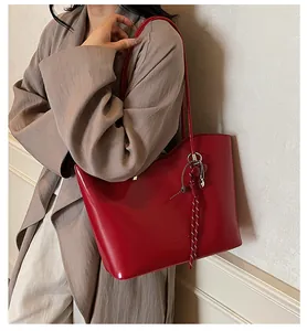 Dettaglio borsa tote in pelle cerata rossa con ciondolo a cuore e logo del marchio