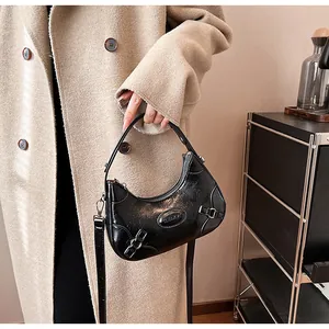 Detail of black glossy pleated shoulder bag with metal logo and sleek half-moon design