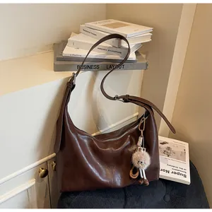 Detail of dark brown leather crescent bag with plush doll charm on a dark chair