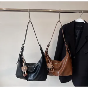 Close-up of black and caramel brown large hobo bags with minimalist texture and plush pendant