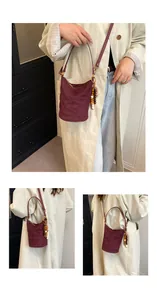 Detailansicht der weinroten Stepp-Eimertasche mit Holzperlen-Anhänger und Schultergurt