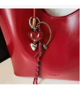 Dettaglio macro della borsa in pelle cerata rossa con ciondoli a cuore e corda intrecciata