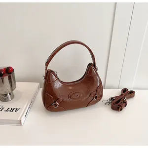 Detail of dark brown glossy hobo bag with adjustable strap and oval logo on white table