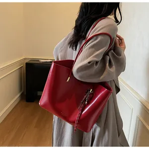 Dettaglio della borsa tote in pelle cerata rossa con hardware dorato e nappa sul modello