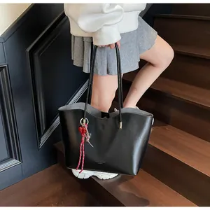Dettaglio della borsa tote in pelle cerata nera con ciondolo a cuore rosso e tracolla