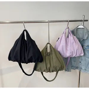 Three pleated crossbody bags in black, olive green, and lavender shown on hangers