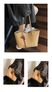 Dettaglio di borsa tote in pelle kaki con ciondolo a cuore e tracolla intrecciata