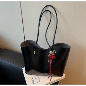 Dettaglio della borsa tote in pelle cerata nera con ciondolo a cuore rosso su libri