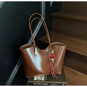 Dettaglio della borsa tote in pelle marrone scuro con bordo ondulato e ciondolo a cuore
