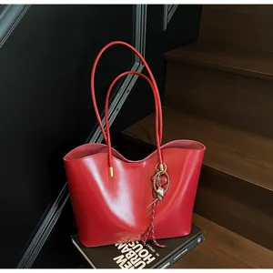 Dettaglio borsa tote in pelle cerata rossa con ciondoli su una scala di legno
