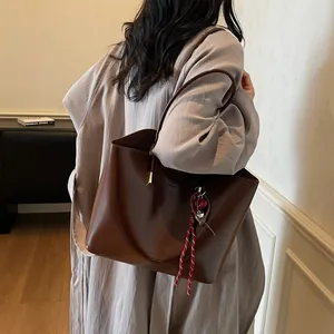 Borsa tote grande in pelle cerata marrone con ciondolo intrecciato indossata da modella