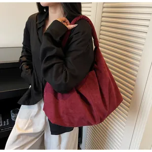 Detail of burgundy suede hobo bag with knotted shoulder strap worn by a model