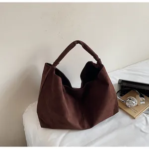 Detail of a large dark brown suede hobo bag with a soft pleated shoulder strap handle