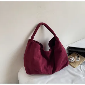 Detail of burgundy suede tote bag with laptop and headphones on a white cushion