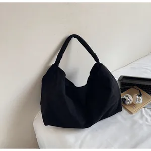 Close-up of a large black canvas tote bag with wide straps in a minimalist setting