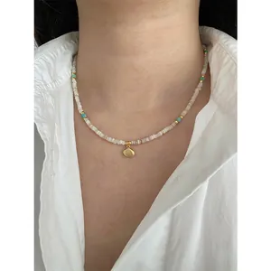 Elegant beaded shell necklace with turquoise accents worn by model over a white shirt