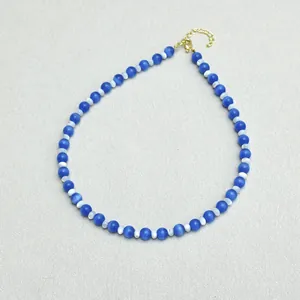 Dettaglio di perle occhio di gatto blu e perline bianche su collana con chiusura a moschettone oro