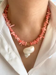 Detail van roze koraal kralenketting met een grote witte schelp hanger bij het model
