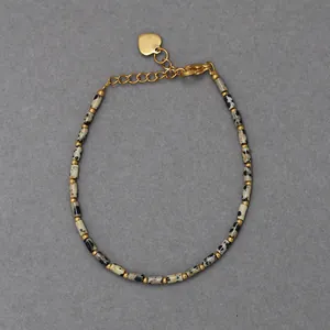 Macro detail of natural dalmatian jasper beads and golden heart charm on a beaded bracelet
