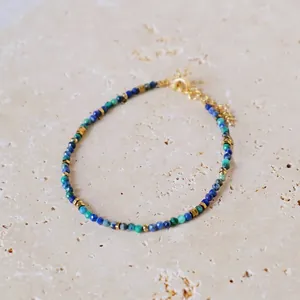 Detail of bohemian natural stone bracelet with gold beads and lobster clasp on stone surface