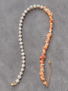 Dettaglio della collana asimmetrica con perle bianche, pietre arancioni e tocchi d'oro