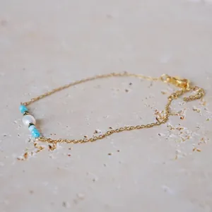 Detail of 18k gold plated chain with white pearl and blue beads on marble